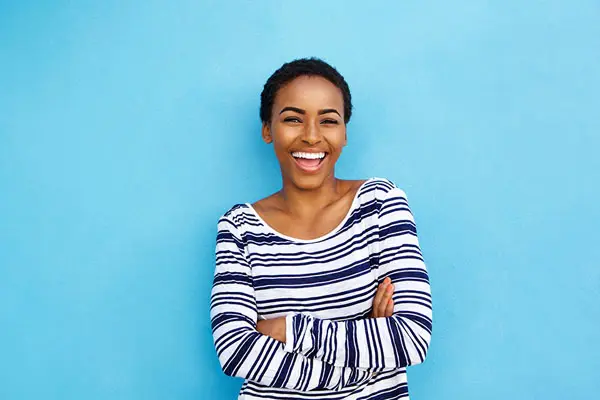 young woman in striped shirt smiling with her new porcelain veneers in front of a blue background